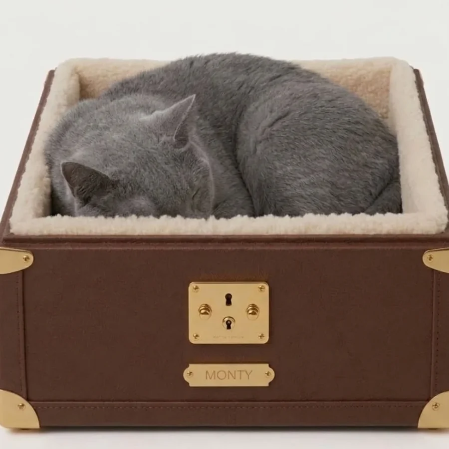 Monty cat bed in tan canvas with brass corners and cream shearling lining, three-quarter view on a pale studio background