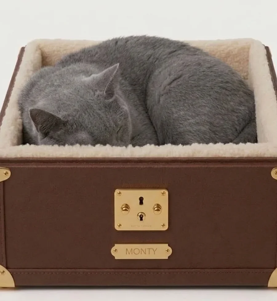 Monty cat bed in tan canvas with brass corners and cream shearling lining, three-quarter view on a pale studio background